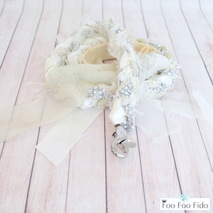 May include: A white dog leash with a silver clasp, made of braided fabric and embellished with rhinestones. The leash is coiled and tied with a white ribbon.