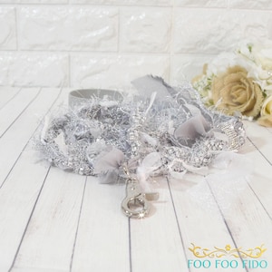 May include: A silver-toned pet leash featuring a mix of metallic fringe, shimmering fabric ribbons, and a sparkling rhinestone-encrusted section. The leash includes a polished metal swivel snap hook at the end for secure attachment to a collar.