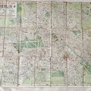 May include: Vintage map of Berlin, Germany, with detailed street layouts and landmarks. The map is folded and shows signs of age, with a faded color palette of greens, browns, and whites. The title "PHARUS-PLAN BERLIN" is visible in the upper left corner.