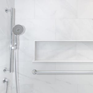 May include: A modern bathroom shower with white marble tile walls. A chrome shower head and a grab bar are mounted on the wall. A recessed shelf is built into the wall. The shower fixtures are chrome.