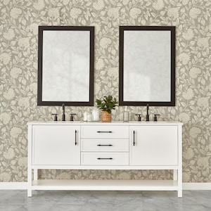 Könnte beinhalten: Ein weißer Badezimmerwaschtisch mit schwarzen Armaturen und zwei rechteckigen Spiegeln mit schwarzen Rahmen. Der Waschtisch hat ein unteres Regal und einen floralen Tapetenhintergrund. Eine kleine Pflanze und Toilettenartikel stehen auf dem Waschtisch.
