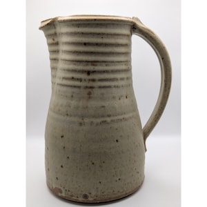 Puede incluir: Una taza de cerámica blanca con un asa negra y el texto "But First, Coffee" en negro y negrita. La taza está sobre una superficie blanca. La taza mide aproximadamente 10 cm de alto.