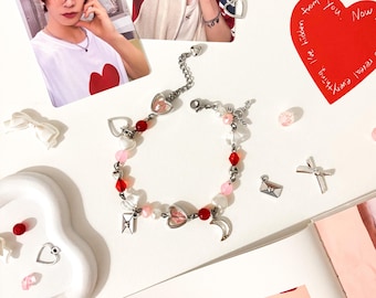 May include: A silver bracelet with red and pink beads, heart-shaped charms, and a crescent moon charm. The image also includes photos of a person, a red heart-shaped card, and small decorative elements.