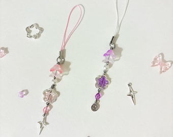 May include: Two beaded phone charms with pink and purple accents. Each charm features a star-shaped pendant and a dangling star charm. Scattered around are star and bow-shaped charms.
