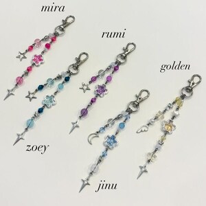 May include: Five beaded keychains with silver-tone clasps. Each keychain features a different color scheme of beads, stars, and flower charms. The keychains are labeled "mira", "zoey", "rumi", "jinu", and "golden".