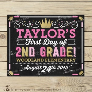 May include: A black chalkboard-style sign with pink and gold text reading "TAYLOR'S First Day of 2ND GRADE!". The sign also includes "WOODLAND ELEMENTARY" and "August 24th 2015". Decorative crowns and flourishes are included in the design.