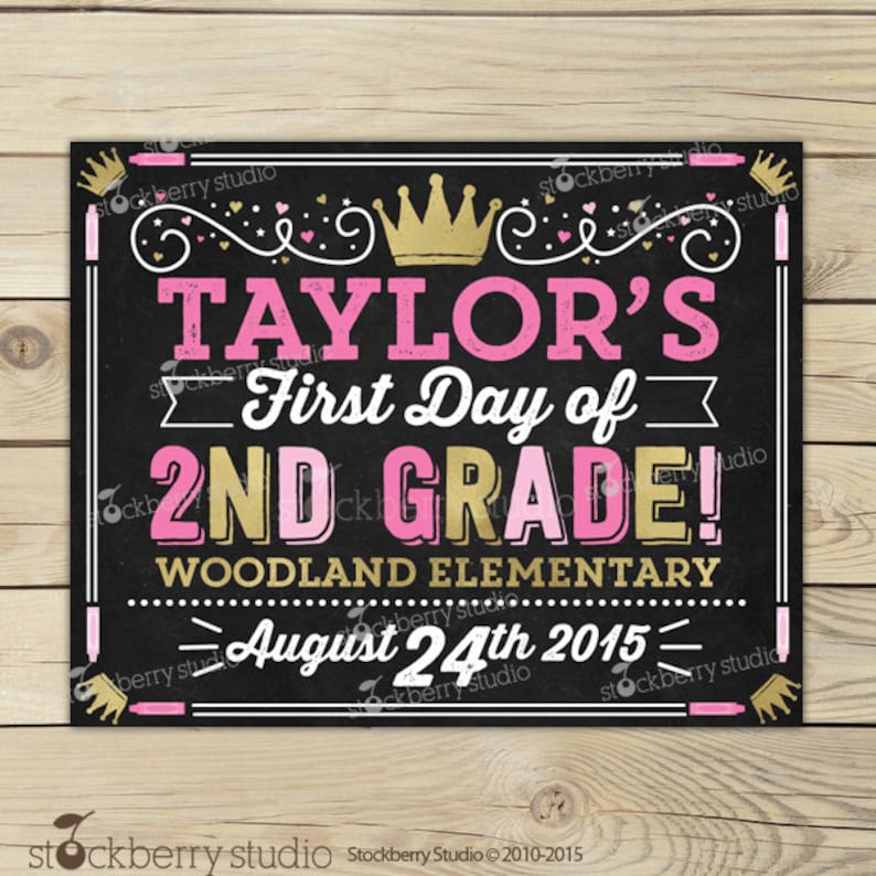 May include: A black chalkboard-style sign with pink and gold text reading "TAYLOR'S First Day of 2ND GRADE!". The sign also includes "WOODLAND ELEMENTARY" and "August 24th 2015". Decorative crowns and flourishes are included in the design.