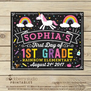 May include: A black chalkboard-style sign with the text "SOPHIA'S First Day of 1ST GRADE" in colourful letters. The sign includes a rainbow, a unicorn, and the date August 21st, 2017. The sign is decorated with stars and school-themed illustrations.