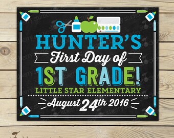 以下が含まれることがあります： 青と緑で「HUNTER'S First Day of 1ST GRADE!」と書かれた黒板風のサイン。学校をテーマにしたイラストと2016年8月24日の日付が含まれています。サインは白い枠で囲まれています。