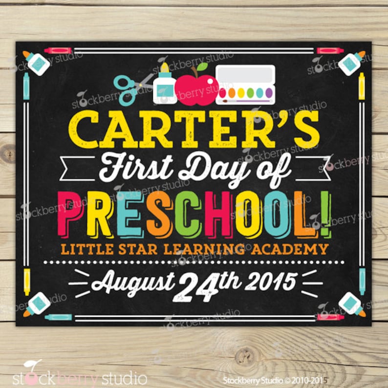 May include: A chalkboard-style sign with the text "CARTER'S First Day of PRESCHOOL!" in colourful letters. The sign includes school-themed illustrations and the date "August 24th 2015". The background is black with a white border.