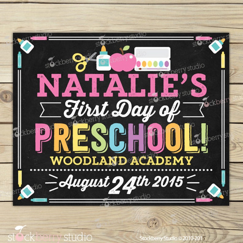 May include: A black chalkboard sign with the text "NATALIE'S First Day of PRESCHOOL!" in various colours. The sign includes school-themed illustrations and the date August 24th, 2015. The sign is framed with white lines and colourful accents.