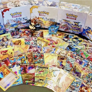May include: A collection of Pokémon trading cards, featuring various characters and designs. Several unopened booster boxes are visible in the background, with text including "Sun & Moon" and "Break Through". The cards display vibrant colors and holographic effects.