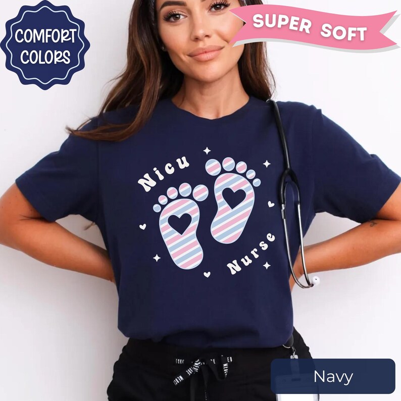 May include: A navy blue t-shirt featuring the text "Nicu Nurse" and a graphic of two baby footprints with heart-shaped cutouts. The footprints are filled with a diagonal striped pattern in light blue, pink, and white. Small white stars and hearts surround the footprints.