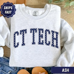 May include: A light gray crewneck sweatshirt featuring the text CT TECH in dark blue block letters with a white polka dot pattern. The garment has long sleeves, a ribbed collar, and a Gildan brand label visible at the inner neckline.
