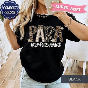 May include: A black t-shirt featuring the text PARA in large letters with a leopard print and checkered pattern, and the word professional in white script below. The design includes small star and smiley face icons and a bow graphic.