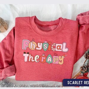 May include: A scarlet red crewneck sweatshirt featuring the text Physical Therapy in a playful, rounded font. Each letter is designed to resemble a colorful Christmas ornament in shades of pink, orange, teal, and red, with festive holiday motifs.