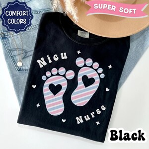 May include: A black t-shirt featuring the text "Nicu Nurse" in white lettering. The design includes two baby footprints with a pink, blue, and white striped pattern and a heart-shaped cutout in the center of each foot, surrounded by small white stars and hearts.