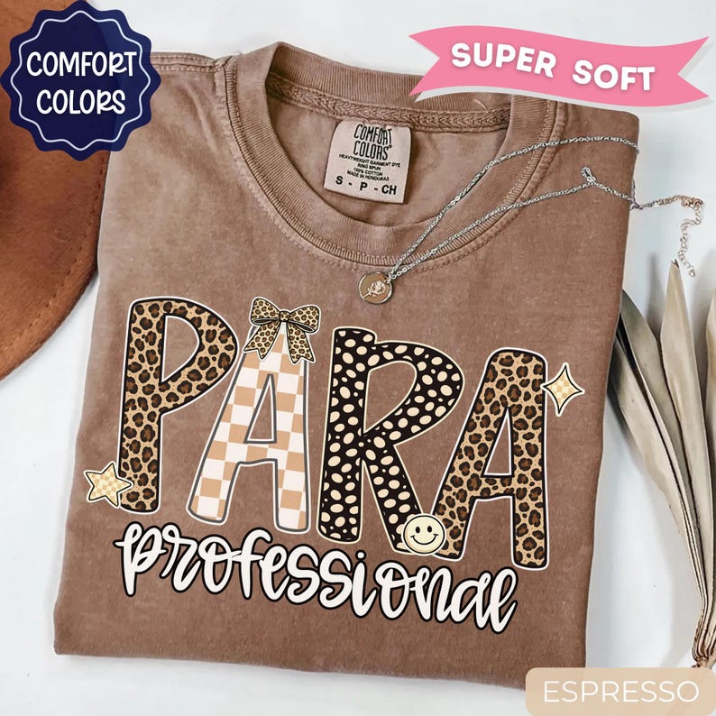 May include: A brown Comfort Colors t-shirt featuring the text PARA in large letters with leopard print and checkered patterns, a small bow, and a smiley face. Below, the word professional is written in white script. Includes a silver necklace.
