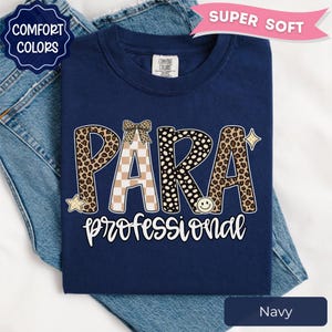 May include: A navy blue t-shirt featuring the text PARA in large letters with leopard print, checkered, and polka dot patterns, topped with a small bow. Below, the word professional is written in white script. Includes star and smiley face icons.