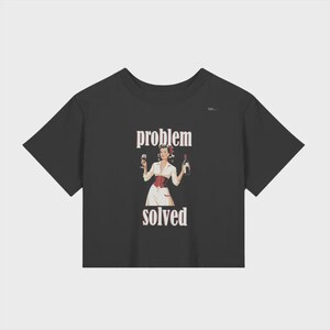 Puede incluir: Top corto negro con las palabras "problem solved" en texto blanco. El gráfico presenta una ilustración vintage de una mujer sosteniendo una copa de vino y una botella de vino. La mujer lleva una blusa blanca, un corsé rojo y una falda blanca.