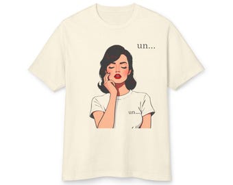 May include: Cream-colored t-shirt featuring a retro illustration of a woman with dark hair and red lipstick, touching her face. The text "un..." is printed above and below the illustration. A casual, everyday tee.