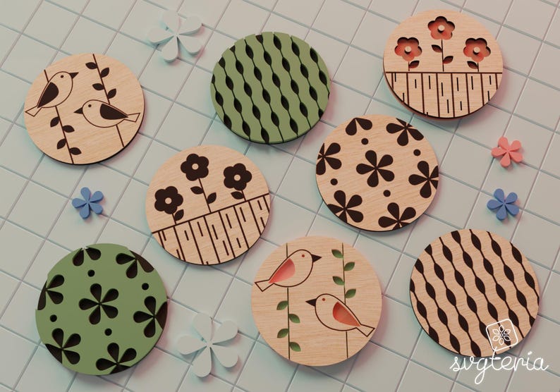 May include: A collection of round wooden coasters with various designs. Some feature birds, flowers, and geometric patterns in black, green, and pink. The coasters are arranged on a light blue tiled surface, with decorative flower accents.