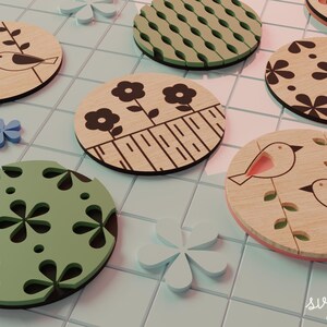 May include: A collection of wooden coasters with various designs, including birds, flowers, and geometric patterns. The coasters are round and feature a natural wood grain with black and green accents. Decorative floral and bird accents are also present.
