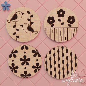 May include: Four round wooden coasters with engraved designs. One coaster features two birds on a branch, another has flowers, a third has a floral pattern, and the last has an oval pattern. The coasters are light brown.