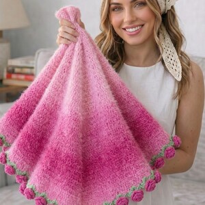 May include: A handmade, pink and fuchsia ombre blanket with a textured, fluffy appearance. The blanket is trimmed with green and pink rose-shaped embellishments. The blanket is held up in front of a person.