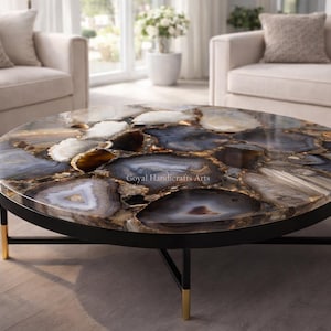 May include: A round coffee table with a polished agate stone top in shades of blue, brown, and white. The table has a black metal frame with gold-colored accents on the legs. The table is a decorative piece of furniture.