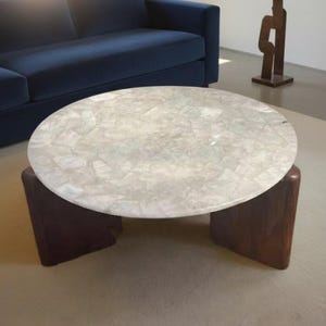 May include: A circular coffee table with a light mosaic-patterned top and dark wooden legs. The table is in front of a navy blue sofa. A bronze sculpture stands in the background.