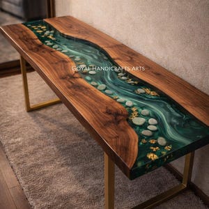 Può includere: Un tavolo a fiume in legno con un fiume in resina epossidica verde scuro. Il tavolo presenta una venatura naturale del legno ed è impreziosito da scaglie d'oro e pietre di fiume. Il tavolo ha gambe in metallo color oro.