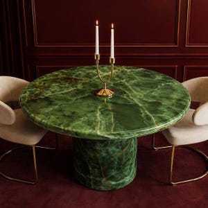 Op de afbeelding: Een ronde groene marmeren tafel met een gouden kandelaar en twee witte kaarsen. De tafel heeft een voetstuk en is omgeven door twee crèmekleurige stoelen met gouden poten. De tafel heeft een diameter van ongeveer 122 cm.