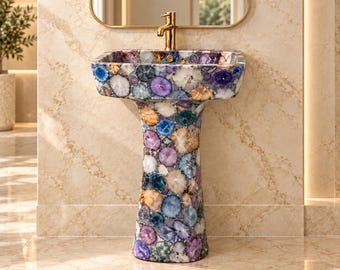 Puede incluir: Un lavabo de pedestal construido con un mosaico de rodajas de ágata pulida en tonos morado, azul, blanco y ámbar. El lavabo presenta una forma cuadrada con esquinas redondeadas y está equipado con un grifo de metal en tono dorado.