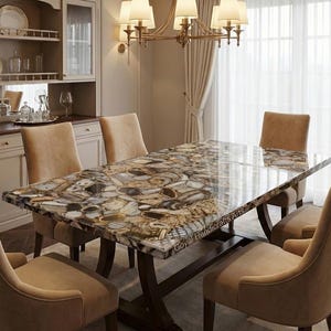 May include: A rectangular dining table with a unique stone top featuring a mosaic of beige, brown, and gray patterns. The table is supported by a dark brown wooden base and surrounded by six beige upholstered chairs. A chandelier hangs above the table.