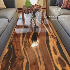 Puede incluir: Una mesa de centro rectangular con una superficie oscura y brillante. La mesa presenta un diseño único con patrones de vetas de madera naturales y fluidos en tonos marrones y beige, encapsulados en una resina transparente. La mesa es una pieza central en una sala de estar.