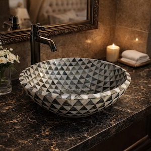 May include: A decorative, round bathroom sink with a geometric pattern of black, white, and gray triangles. The sink is made of a mosaic-like material and sits on a dark countertop. The text "Goyal Handicrafts & Arts" is visible.