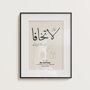 Puede incluir: Impresión artística enmarcada con caligrafía árabe negra sobre fondo beige. La impresión incluye la frase en inglés "Do not fear" y un versículo del Corán. El marco es negro y se muestra en una pared blanca.