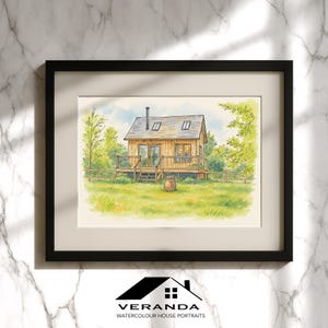 May include: A framed watercolour painting of a small wooden cabin with a deck, a chimney, and two skylights, set in a grassy field with trees. The artwork is presented in a black frame with a cream mount, featuring the text Veranda Watercolour House Portraits.
