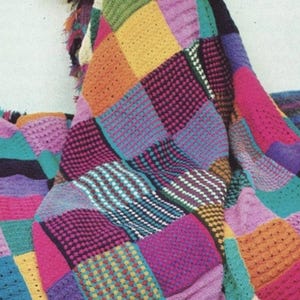 May include: A colorful, handmade crochet blanket with a patchwork design. The blanket features squares of various colors, including yellow, orange, pink, purple, and blue. The texture of the blanket is visible, showcasing the different stitch patterns used.