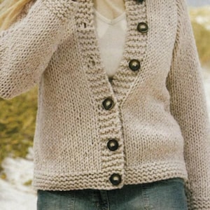 May include: A beige, chunky-knit cardigan sweater with a V-neck and long sleeves. The sweater has large, dark buttons down the front and ribbed detailing at the cuffs and hem. The garment is made of a thick, textured yarn.