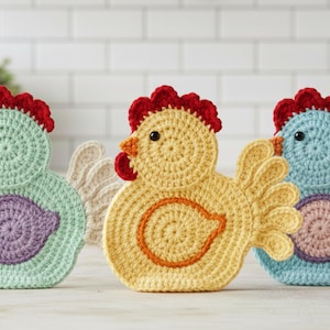 May include: Crocheted chicken-shaped trivets in pastel colors. The trivets feature red combs, orange beaks, and circular bodies with a contrasting oval design. The trivets are in shades of yellow, blue, and green.