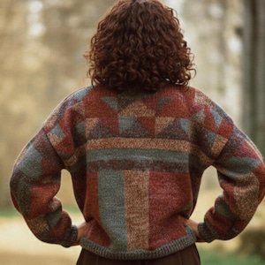 May include: A person wearing a patterned sweater with a geometric design in shades of red, gray, and brown. The sweater has long sleeves and a crew neck. The person is standing outdoors.