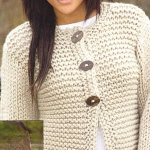May include: A cream-colored, chunky knit cardigan with three large, round, wooden buttons. The sweater has a crew neck and long sleeves. The knit pattern is visible, creating a textured appearance. The cardigan is worn over a white top.