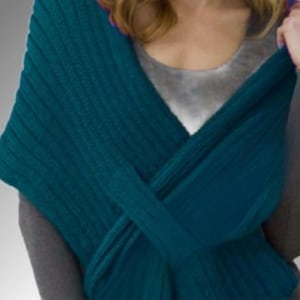 May include: A teal-colored knitted scarf is draped over the shoulders. The scarf is made of a thick, ribbed knit fabric. The scarf is wrapped and crossed in the front. The background is a gradient of gray.