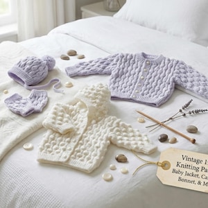 Może przedstawiać: Kolekcja dzianinowych ubranek dla niemowląt w miękkich odcieniach lawendy i kremu, w tym kurtka, kardigan, czapeczka i rękawiczki. Przedmioty ułożone są na białej narzucie z vintage metką z napisem "Vintage 1990s Knitting Pattern: Baby Jacket, Cardigan, Bonnet, & Mitts."