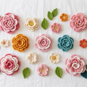 May include: A collection of handmade crochet flowers and leaves in various sizes and colors. The flowers include shades of pink, yellow, orange, and blue, with white and yellow centers. Green leaves are scattered around the flowers, creating a vibrant and textured display.