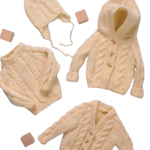 May include: A collection of cream-colored, hand-knitted baby clothing. The set includes a hooded cardigan, a sweater, a cardigan with buttons, and a bonnet. The garments feature a cable knit design and wooden buttons.