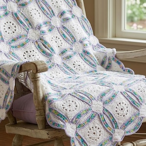 Puede incluir: Una manta blanca de ganchillo con un diseño floral está sobre una mecedora de madera. La manta presenta un patrón repetitivo de círculos y cuadrados, con acentos de azul claro, verde y morado. La manta es suave y acogedora.