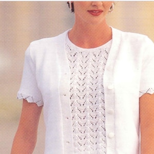 Puede incluir: Un cárdigan blanco de punto con mangas cortas y una camiseta a juego con cuello redondo. La camiseta presenta un patrón calado detallado. El cárdigan tiene una botonadura y bordes festoneados en las mangas.